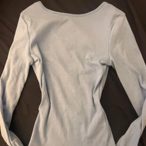 Ljusblå långärmad topp med öppen rygg  -  Lusblå topp från Gina  i storlek XS. Toppen har en snygg scoopad urringning bak och långa ärmar. Materialet är mjuk bomull med stretch. Färgen är mörkare än på bilderna.