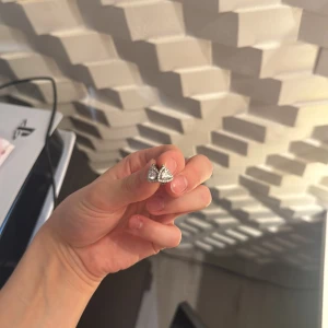 Silverfärgade örhängen med hjärtform - Säljer ett par söta örhängen i silverfärg med gnistrande stenar formade som hjärtan. De har en smidig låsmekanism och passar perfekt för dig som gillar glittriga detaljer och romantisk stil.