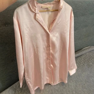 Ljusrosa satinblus från H&M - Supersnygg ljusrosa blus från H&M i glansigt satinmaterial. Blusen har en klassisk krage, knappar framtill och trekvartsärmar. Perfekt för dig som gillar en chic och mjuk vibe. Passar dig som vill sticka ut med en feminin touch.