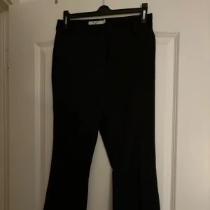 Svarta kostymbyxor från NA-KD - Stilrena svarta kostymbyxor från NA-KD med klassisk rak passform och hällor för bälte. Perfekta för en clean look och funkar till många olika outfits. Materialet känns mjukt och följsamt, och byxorna har en tidlös design.