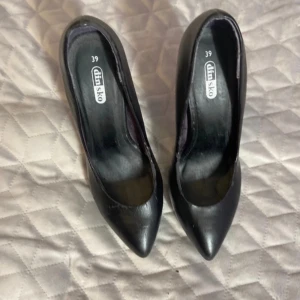 Svarta pumps från Din Sko, storlek 39 - Snygga svarta pumps från Din Sko i storlek 39. Skorna har spetsig tå, hög klack och en stilren, klassisk form. Tillverkade i skinnimitation med platt sula framtill och elegant finish. Perfekta för dig som gillar en chic och tidlös look.knappt använda.