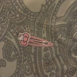 Hello Kitty rosa hårspänne - Sött hårspänne i ljusrosa med en stor Hello Kitty-dekoration framtill. Spännet har en klassisk klick-modell och är perfekt för att hålla håret på plats med en gullig touch. Passar dig som gillar kawaii-stil och vill ha något extra i håret.