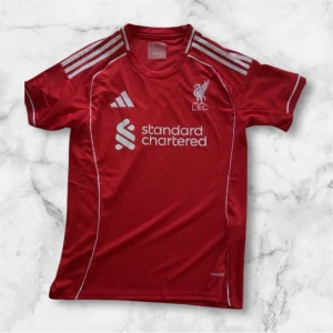 Liverpool röd fotbollströja Adidas - Säljer en röd Liverpool fotbollströja från Adidas med vita detaljer och logga på bröstet. Tröjan har korta ärmar, rund hals och är tillverkad i ett lätt, ventilerande material. Standard Chartered tryck på framsidan och klassiska Adidas-ränder på axlarna.