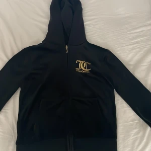Svart Juicy Couture hoodie  - Svart hoodie från Juicy Couture med dragkedja och guldiga tryck på bak och fram sidan. Trycket är slitet där bak annars ser jag inga tecken på slitenhet. 