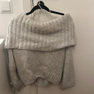Grå stickad offshoulder tröja - Supermysig grå stickad tröja med bred offshoulder-krage och ribbade detaljer. Långärmad och loose passform, passar till jeans eller kjol.