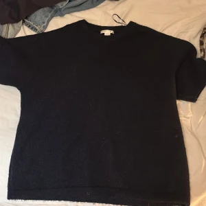 Svart stickad tröja från Gina Tricot - Mysig svart stickad tröja från Gina Tricot i storlek M. Tröjan har en enkel, rak passform med rund hals och korta ärmar. Perfekt för lager-på-lager och chill dagar. Materialet är mjukt och fluffigt, vilket gör den extra skön att bära.