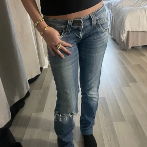 Lågmidjade Lee jeans  - Säljer ett par blå jeans från Lee med slitning och fransar vid ena knät. Jeansen har låg midja och raka ben. 💞Står 13Y men skulle säga att de är likadana som en w25💓