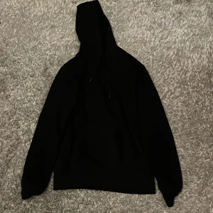 Svart hoodie från cubus - Svart hoodie från Cubus med klassisk passform och huva med snörning. Tröjan har långa ärmar och är tillverkad i mjuk bomullsmix, perfekt för en chill och stilren look. Diskret logga i nacken. Enkel att matcha med allt.