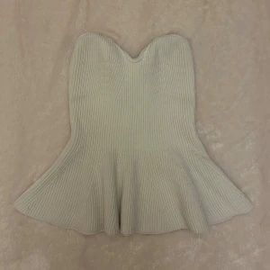 Beige ribbad bandeau tubtopp - Säljer en beige bandeau tubtopp med snygg ribbad struktur och utsvängd nederkant. Toppen är axelbandslös och har en hjärtformad överkant som ger en cool siluett. Har en fläck, se andra bilden. Har inte försökt få bort fläcken. 