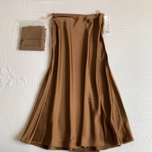 Brun satin kjol från Uniqlo - Säljer en snygg brun satin kjol från Uniqlo. Perfekt att styla med sneakers eller boots för en chill look.