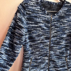 Blåmönstrad stickad kavaj  - Säljer en blåmönstrad kavaj med grov stickad struktur och dragkedja framtill. Jackan har ett coolt mönster, rund hals och två fickor med dragkedja. Perfekt för dig som gillar att vara fin och samtidigt bekväm.