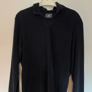 Svart pikétröja i frotté från H&M - Svart långärmad pikétröja från H&M i mjuk frotté. Klassisk krage och relaxed passform, perfekt för en chill och stilren look. Enkel och clean design utan knappar framtill.