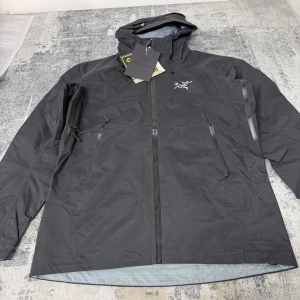 Svart lightweight jacka från Arc'teryx - Säljer en svart vindjacka från Arc'teryx med huva och flera praktiska dragkedjefickor. Jackan har en stilren design med Arc'teryx-logga på bröstet och är tillverkad i slitstark syntet. Perfekt för dig som gillar friluftsliv och vill ha en jacka med grym passform.