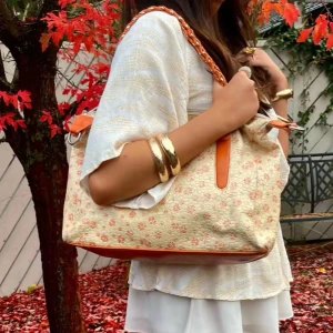 Blommig axelremsväskan  - Super fin axelremsväska med små blommor på! Både blommorna och detaljerna går emot de orangea! Tre stycken innerfack, perfekt både till sommaren och höst!🍁tyvärr ett litet håll i ena innerfack…