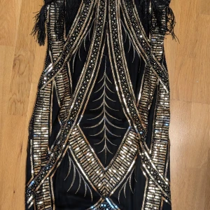 Svart Gatsby-klänning - Säljer en svart Gatsby-klänning med paljetter och fransar. Halterneck. Aldrig använd. Köpt till en fest som aldrig blev av. Storlek L.