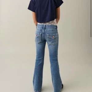 Blå bootcut jeans med fickdetaljer - Snygga blå jeans med bootcut passform och markerade bakfickor med lock och knappdetaljer. Jeansen har klassisk femficksdesign och kontrastsömmar som ger en cool vintagekänsla. Perfekta för dig som gillar en retrostil.