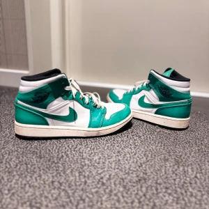 Nike Air Jordan 1 Mid grön/vit - Säljer ett par Nike Air Jordan 1 Mid i fräscha gröna och vita färger. Skorna har klassisk snörning, svart yttersula och ikoniska Jordan Wings-loggan på sidan. Tillverkade i skinn med vit bas och gröna paneler, samt svart foder och detaljer. För att göra skorna fräschare läggtill nya snören. 