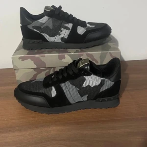 Valentino Rockrunner sneakers camo - Snygga Valentino Rockrunner sneakers med svart, grå och vit camouflage-mönster. Skorna har svarta detaljer i skinn och mocka, samt snörning och platt sula. Perfekta för dig som vill sticka ut med en exklusiv streetstyle.