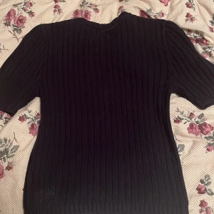 Svart ribbad stickad tröja - Svart stickad tröja med ribbat mönster och kortare ärmar. Tröjan har en klassisk rund halsringning och är perfekt för dig som gillar en enkel men stilren look. Passar bra till både jeans och kjol.