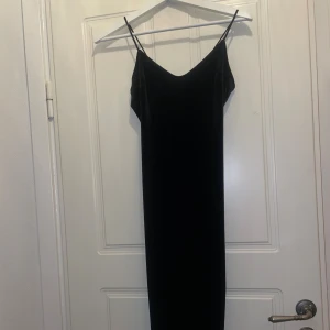 Svart lång sammetsklänning NLY One - Supersnygg svart långklänning från NLY One i mjuk sammet. Klänningen har smala axelband, v-ringad urringning och meshdetalj framtill. Perfekt för dig som gillar stilrena och eleganta plagg med lite edge.