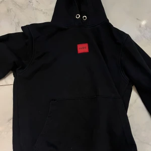 Svart hoodie  - Svart hoodie. Tröja har huva med metallöljetter och en stor magficka framtill. Perfekt för dig som gillar stilren streetwear med en touch av färg.