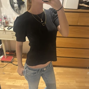 Svart topp med puffärm från Pieces - Svart topp från Pieces i storlek M med korta puffärmar och rund hals. Materialet är ribbad och ger en snygg struktur. Passformen är normal och toppen är enkel att styla med jeans eller kjol. Perfekt för dig som gillar stilrena och trendiga plagg.