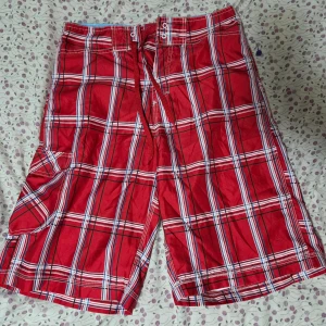 Röd-rutiga shorts från HotepH - Säljer ett par röda rutiga shorts från HotepH med vita och svarta linjer. De har snörning i midjan och en praktisk sidoficka. Perfekta för sommardagar och har en avslappnad passform. Materialet känns lätt och svalt.