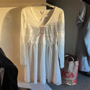 Vit spetsklänning från Bubbleroom oanvänd - Superfin vit kortklänning från Bubbleroom med långärmade spetsärmar och v-ringning framtill. Överdelen är i spets med diskret mönster och kjolen är slät och flowy. Dragkedja i sidan för enkel påklädning. Perfekt för student eller sommarens tillfällen! Helt oanvänd och helt ny😍