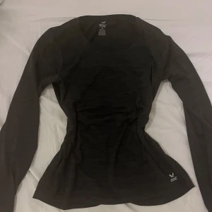 Svart tajt långärmad träningströja SOC - Svart långärmad träningströja från SOC med rund halsringning och diskret logga framtill. Tröjan är figurnära och har en reflekterande detalj på ryggen. Perfekt för löpning eller gympass. Materialet är mjukt och stretchigt för maximal rörelsefrihet.