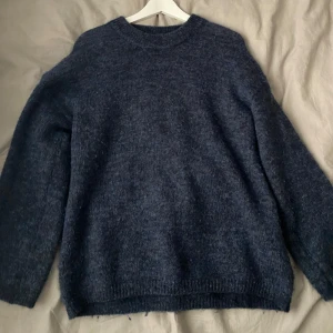 Mörkblå stickad tröja med rund hals - Mysig mörkblå stickad tröja med rund halsringning och långa ärmar. Perfekt för kyliga dagar och enkel att matcha med jeans eller kjol. Tröjan har en lite oversized passform och ribbade muddar vid ärmslut och nederkant. Den är i storlek xs men sitter väldigt snyggt på mig som vanligtvis har S-M