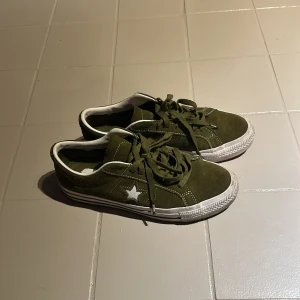 Olivgröna Converse CONS sneakers - Säljer ett par olivgröna Converse CONS sneakers i mocka med vit sula och vita detaljer. Skorna har snörning, vit stjärna på sidan och klassisk logga bak. Perfekta för dig som gillar streetstyle och vill ha något som sticker ut. Ändast använda ett fåtal gånger! Pris går att diskutera. Nypris 990kr
