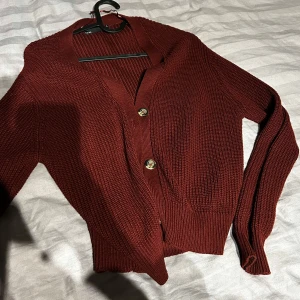 Vinröd kofta från 157, XS - Snygg vinröd kofta från 157 i stickad bomull. Modellen har långa ärmar, ribbade muddar och guldiga knappar framtill. Perfekt för lager-på-lager och passar till både jeans och kjol.