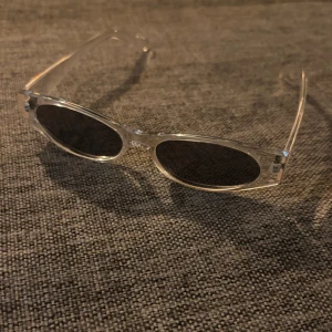 Transparenta ovala solglasögon - Snygga solglasögon med transparent båge och ovala, mörka glas. Ramen är i plast och ger en modern och clean vibe. Perfekta för dig som vill sticka ut med en stilren accessoar.