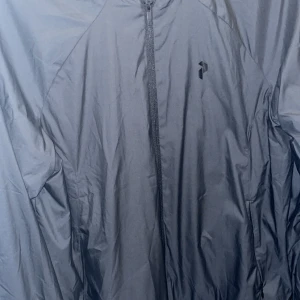 Svart vindjacka Peak Performance S - Svart vindjacka från Peak Performance i storlek S. Jackan har hel dragkedja framtill, diskret logga på bröstet och meshfoder på insidan för extra komfort. Lätt och smidig modell med klassisk passform. Aldrig använd bara testad utan prislapp!