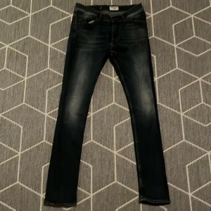 Tiger of Sweden mörkblå jeans - Snygga mörkblå jeans från Tiger of Sweden med klassisk femficksdesign och läderpatch bak. Jeansen har smal passform och diskreta slitningar för en cool look. Perfekta för dig som gillar stilrena och moderna jeans.