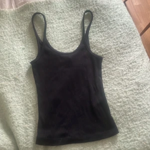 Svart ribbad linnetopp från H&M XS - En svart ribbad linnetopp från H&M i storlek XS. Toppen har smala axelband och är figurnära med stretchigt material. Perfekt att styla med jeans eller kjol för en enkel och snygg look.
