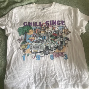 Vit t-shirt Brandy Melville med tryck - Vit t-shirt från Brandy Melville i 100% bomull med färgglatt tryck framtill. Motivet visar en tecknad bil, palmer och texten 'CHILL SINCE 1993 PARIS'. Klassisk baggy passform och korta ärmar, perfekt för en avslappnad stil. Skulle säga att storleken är xs-m