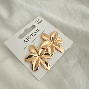 Guldiga örhängen  - Stora, blommiga örhängen i blank guldfärg. De har en stilren och trendig design, samt helt oanvända! 