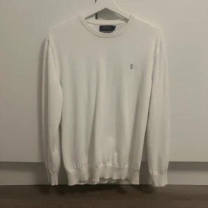 Vit bomullströja från Polo Ralph Lauren - Klassisk vit tröja från Polo Ralph Lauren i 100% pima bomull. Tröjan har rund halsringning, långa ärmar och den ikoniska broderade loggan på bröstet. Perfekt basic med stilren look och ribbade muddar vid ärmslut och nederkant.