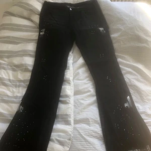 Svarta bootcut jeans med stänk från Romwe - Svarta jeans från Romwe i bootcut-modell med vita färgstänk och små håldetaljer längs benen. Snyggt street-inspirerat stuk och raka ben som blir vidare nertill. Perfekta för dig som gillar en edgy look.