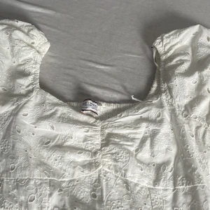 Vit kortklänning från Lily & White - Supersöt vit kortklänning från Lily & White med puffärmar och broderade blommor över hela klänningen. Klänningen har en rundad halsringning och är gjord i bomull, vilket gör den både bekväm och fräsch. Perfekt för sommarens alla tillfällen!