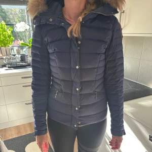 Mörkblå Parajumpers dunjacka med pälskrage - Säljer denna jättefina mörkblåa dunjackan ifrån Parajumpers med fluffig pälskrage på huvan. Pälsen på luvan är avtagbar. Köpt ifrån NK för 7000 kr och använt ett fåtal antal gånger och är i ett väldigt fint skick med lite tecken på användning som inte är synligt.