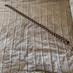 Flätat bälte i skinn med färgdetaljer - Säljer ett snyggt flätat bälte med brunt skinn och inslag av blått och gult från ett exklusivt märke från Italien.  Bältet har ett coolt mönster med färgade remsor som ger en unik look. Perfekt för att lyfta din outfit med lite extra färg och stil.