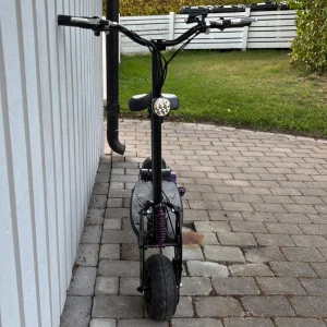 Elektrisk Scooter med Sadel - Kraftfull elektrisk scooter med breda däck, stötdämpare fram och bak, och bekväm sadel. Utrustad med LED-strålkastare och skivbromsar. Svart och lila detaljer. Skicket är gott, däcken är bra Perfekt för bekväm och snabb pendling.