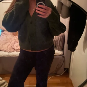 Mörkgrön stickad kofta från Weekday - Mysig mörkgrön stickad kofta från Weekday i storlek S. Koftan har en croppad passform, stora knappar framtill och långa ärmar. Perfekt för lager-på-lager och chill dagar. Snygg att styla med både jeans och kjol.