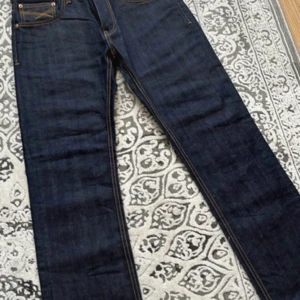 Mörkblå jeans från Pace W30 L32 - Snygga mörkblå jeans från Pace med klassisk femficksdesign och kontrastsömmar i gult. Jeansen har rak passform och är tillverkade i robust denim. Märkespatch baktill i svart och röd logga på insidan av linningen. Perfekta för dig som gillar stilrena och tidlösa jeans.