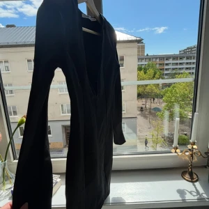 Svart långärmad kortklänning  - En stilren svart kortklänning  med lång ärm och figurnära passform. Klänningen har en djup v-ringning framtill och är sydd i ett mjukt, stretchigt material som sitter snyggt på kroppen. Perfekt för dig som gillar minimalistisk och clean stil. Använd en gång på nyår! 