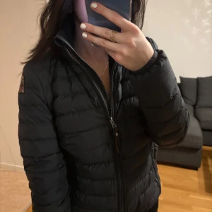 Svart dunjacka från Parajumpers - Säljer en svart dunjacka från Parajumpers med klassisk patch på ärmen. Jackan har quiltad design, hög krage och dragkedja framtill. Perfekt för kyliga dagar och riktigt snygg till streetwear-looken.🤍