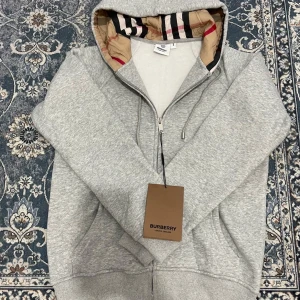 Grå Burberry hoodie - Snygg grå hoodie från Burberry med klassiskt rutigt foder i huvan. Tröjan är nyskick 