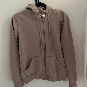 Beige hoodie med dragkedja XS - Säljer en beige hoodie från H&M i storlek XS. Tröjan har huva med snörning, dragkedja framtill och två stora fickor. Perfekt för chill dagar och enkel att matcha med jeans eller mjukisbyxor.